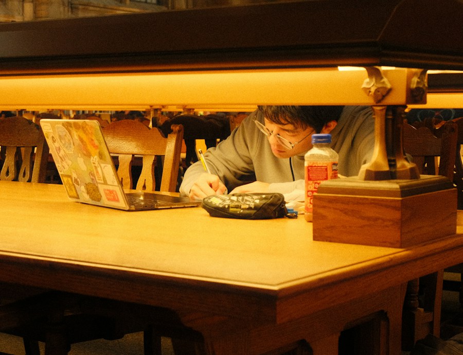 Un étudiant travaille à la bibliothèque avec son ordinateur et ses notes.